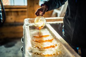 A close-up of a person at sugar shack pouring maple syrup onto snow to make maple sugar taffy.