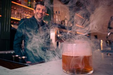 Bartender standing behind bar with cocktail on counter