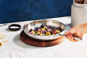 Hand placing a Tramontina Stainless Steel Tri-Ply10-Inch Fry Pan on a wood trivet