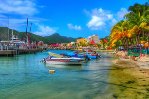 Colorful boats, palm trees, and a mountain backdrop showing St Maarten