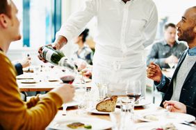 Waiter interacting with couple and pouring wine at dining table