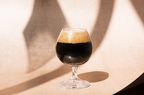 A glass of dark beer, on a beige background with shadows.