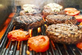 hamburger meat cooking on the grates of a grill in close-up with tomatoes